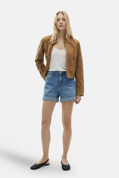 Short en denim bleu moyen de MANGO, porté avec un débardeur blanc et une veste marron.