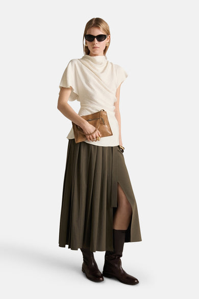 Beige blouse met korte mouwen van MANGO, gedragen met een groene plooirok en bruine leren laarzen.