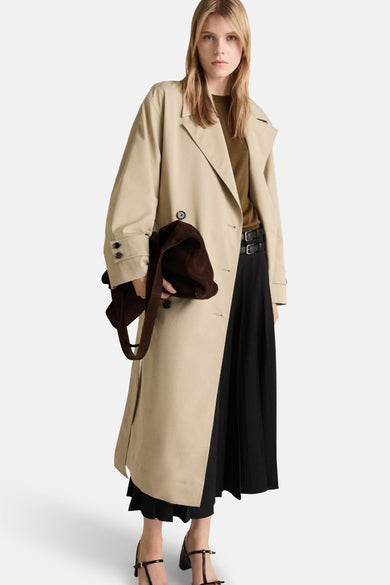 Lange beige jas van MANGO, gedragen over een zwarte jurk, met een bruine tas en zwarte hak sandalen.
