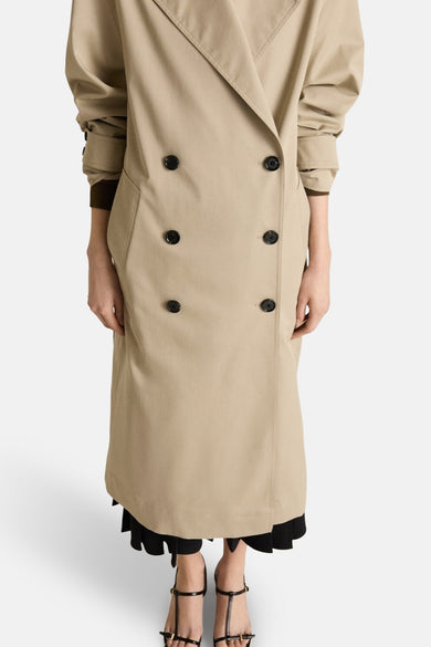 Lange beige jas van MANGO, dubbele rij knopen met zwarte knopen en zwarte schoenen met bandjes.