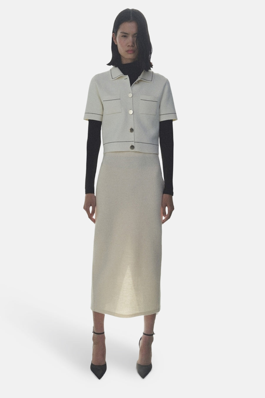 Ecru gilet MANGO, gedragen over een zwarte coltrui met een bijpassende kokerrok en naaldhakpumps.