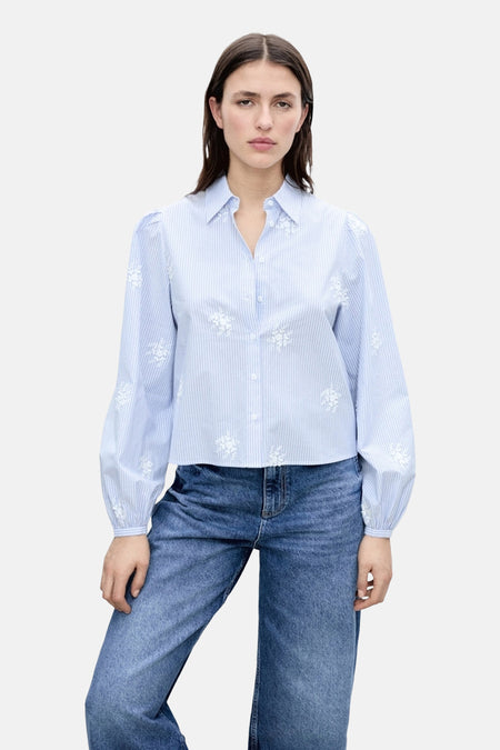 Blauwe blouse met lange mouwen en strepen van MANGO, versierd met witte bloemenborduursels, gedragen met een wijde spijkerbroek.