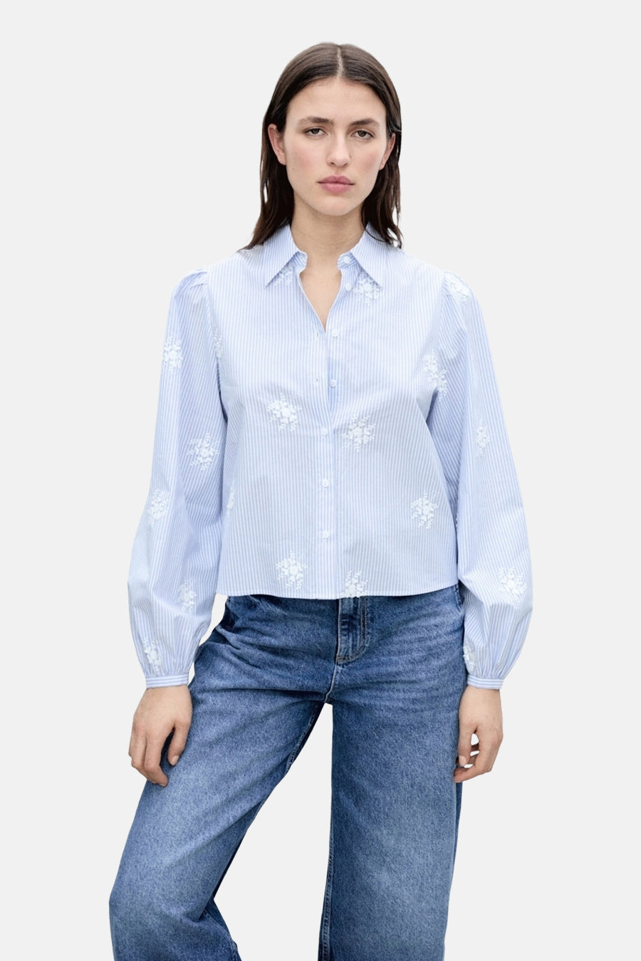Chemise rayée bleue à manches longues de MANGO, ornée de broderies florales blanches, portée avec un jean.