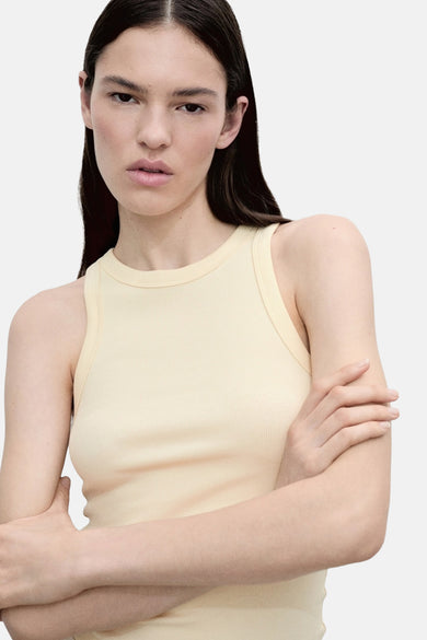 Gele tanktop van MANGO, met los bruin haar en een witte broek.