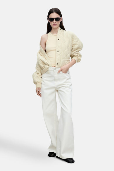 Gele tanktop van MANGO, gedragen met een crèmekleurig gewatteerd jack, een witte high-waisted jeans en een zwarte zonnebril.