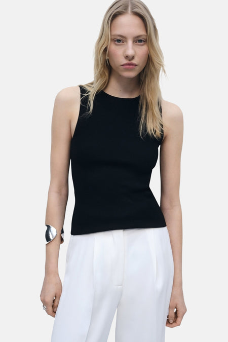 Top noir sans manches de MANGO, porté avec un bracelet argenté et un pantalon blanc.
