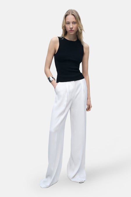 Top sans manches noir de MANGO, porté avec un pantalon blanc ample et un bracelet argenté.
