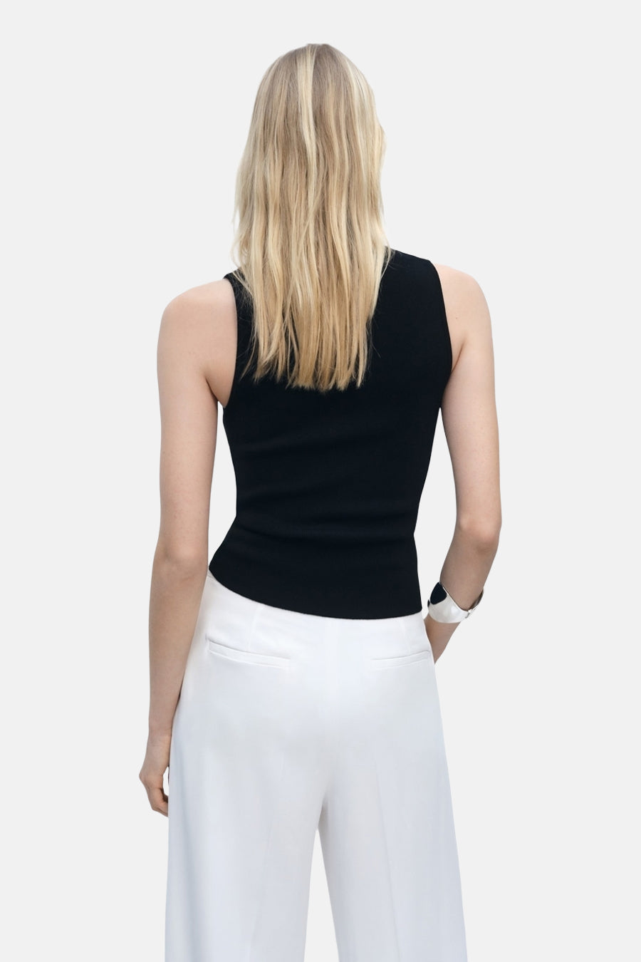 Top noir sans manches de MANGO, porté avec un pantalon blanc taille haute, vue de dos.