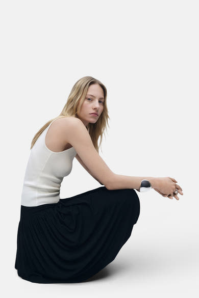 Top écru sans manches de MANGO, porté avec une jupe noire longue et un bracelet argenté.