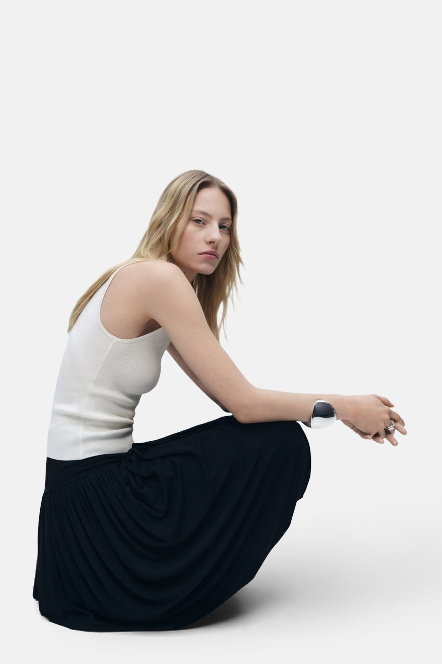 Top écru sans manches de MANGO, porté avec une jupe noire longue et un bracelet argenté.