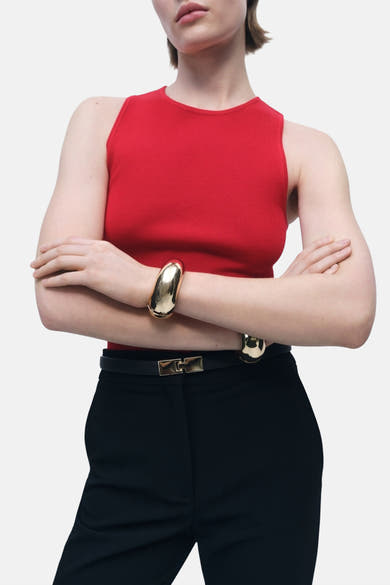 Rood mouwloos topje van MANGO, gedragen met een zwarte broek en een riem met gouden gesp.