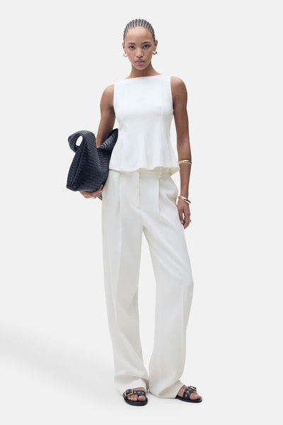 Top blanc sans manches de MANGO, porté avec un pantalon blanc ample et des sandales noires.
