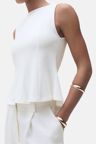 Top sans manches blanc de MANGO, porté avec un pantalon blanc et des bracelets dorés.
