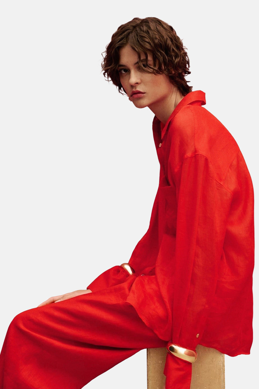 Chemise rouge à manches longues de MANGO, portée avec un pantalon rouge et des bracelets dorés.