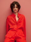 Chemisier rouge à manches longues de MANGO, en lin texturé, porté ouvert sur un fond rose assorti.
