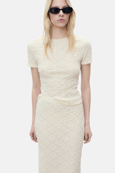 T-shirt écru à manches courtes de MANGO, avec une texture gaufrée, porté avec des lunettes de soleil noires.