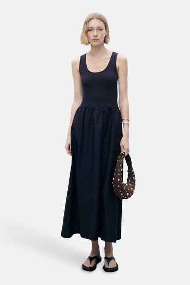 Marineblauwe jurk van MANGO, met een losse pasvorm en een gladde textuur, gedragen met een bruine handtas met studs.