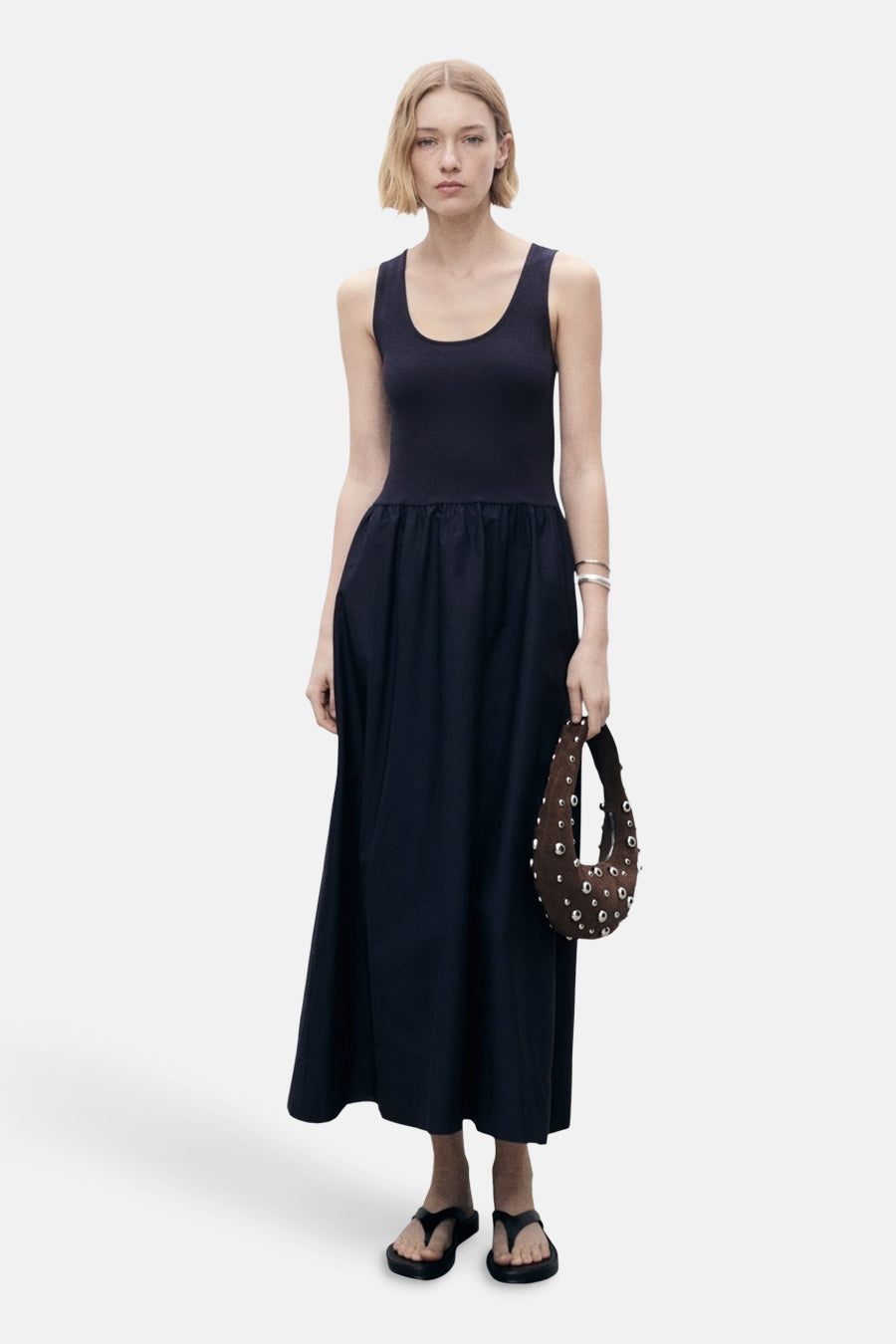 Marineblauwe jurk van MANGO, met een losse pasvorm en een gladde textuur, gedragen met een bruine handtas met studs.