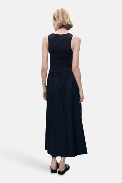 Blauwe jurk van MANGO, lange snit, zilveren armbanddetail, gedragen met zwarte sandalen, van achteren gezien.