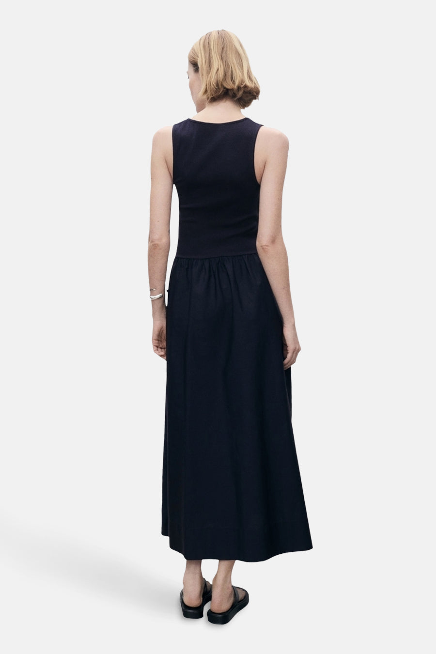 Blauwe jurk van MANGO, lange snit, zilveren armbanddetail, gedragen met zwarte sandalen, van achteren gezien.