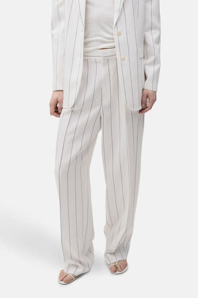Pantalon de costume blanc rayé de MANGO, coupe ample avec des sandales blanches.
