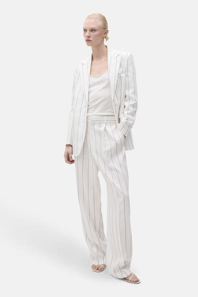 Pantalon de costume blanc de MANGO, à rayures, coupe ample et jambe large, porté avec un débardeur.
