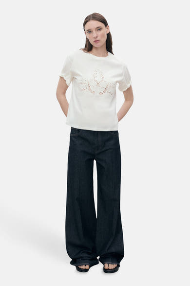 Wit T-shirt met korte mouwen van MANGO, met bloemenkanten detail aan de voorkant, gedragen met een wijde jeans.