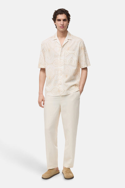 Wit overhemd met korte mouwen van MANGO, met een bloemenpatroon en gedragen met een beige broek en muiltjes.