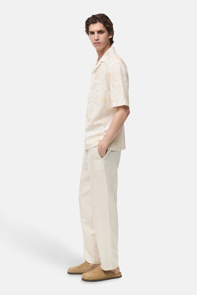Chemise à manches courtes blanche à motif doré par MANGO, portée avec un pantalon en lin écru et des mules en daim.