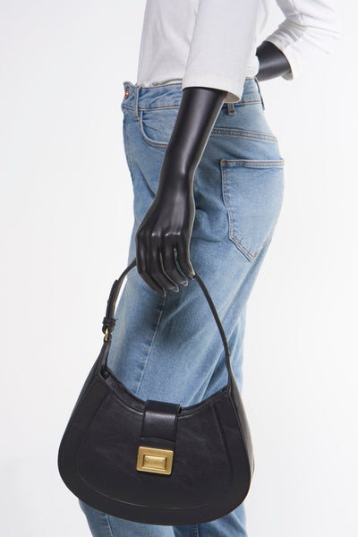 Zwarte schoudertas van MANGO, gedragen door een model met een blauwe jeans en een wit T-shirt, zijwaarts bekeken.