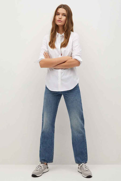 Chemise blanche à manches longues de MANGO, portée avec un jean décontracté et des baskets grises.