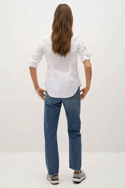 Chemise à manches longues blanche de MANGO, avec des manches retroussées et portée avec un jean.