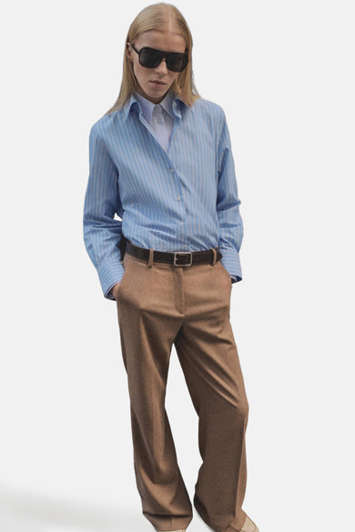 Blauw gestreept overhemd met lange mouwen van MANGO, gedragen met een bruin overhemd en een bruine broek, en een zwarte zonnebril.