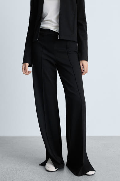 Zwarte broek van MANGO met plooien aan de voorkant en wijde pijpen, gedragen met witte schoenen.