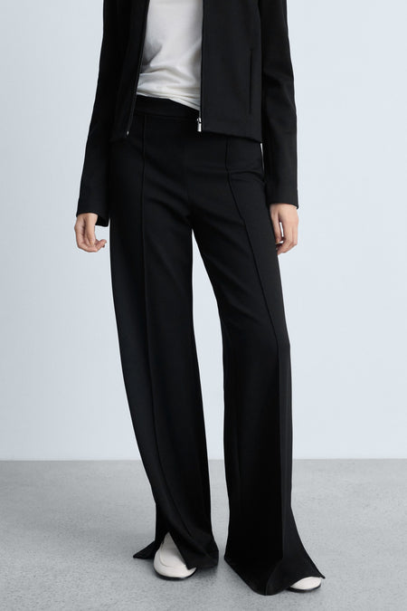 Zwarte broek van MANGO met plooien aan de voorkant en wijde pijpen, gedragen met witte schoenen.