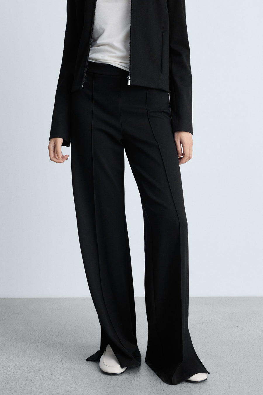 Zwarte broek van MANGO met plooien aan de voorkant en wijde pijpen, gedragen met witte schoenen.