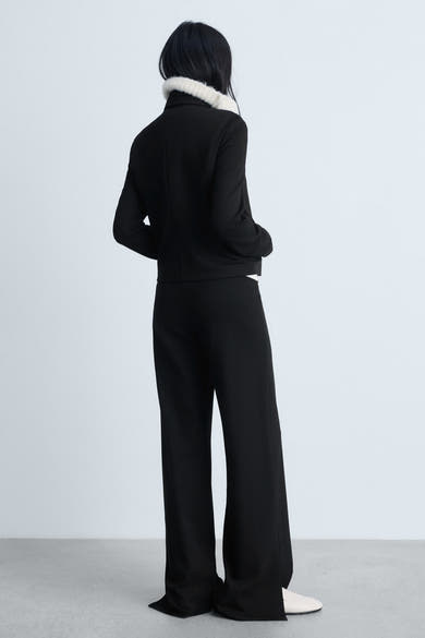 Zwarte broek van MANGO, rechte pasvorm, gedragen met een zwart jasje met imitatiebontkraag.