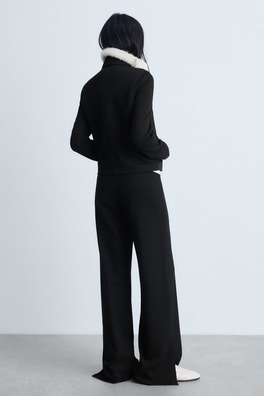 Zwarte broek van MANGO, rechte pasvorm, gedragen met een zwart jasje met imitatiebontkraag.