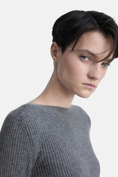 Pull à col rond gris de MANGO, en maille côtelée, porté par une femme au regard intense.