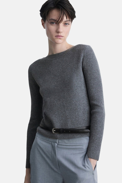 Grijze ronde nekpullover vanANGOANGO, met met een zwarteenur op een donge blauwe broek.