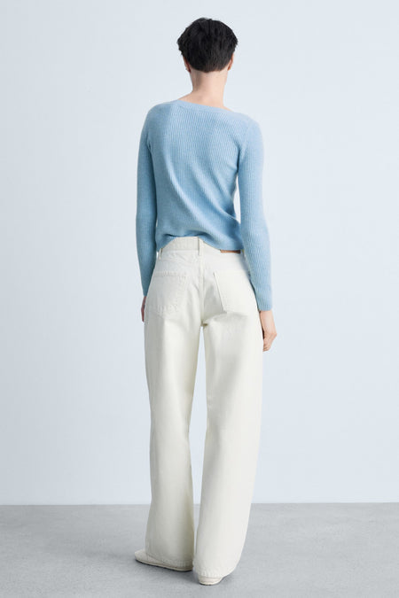 Pull à col rond bleu de MANGO, en tricot côtelé, porté avec un jean blanc à jambes larges.