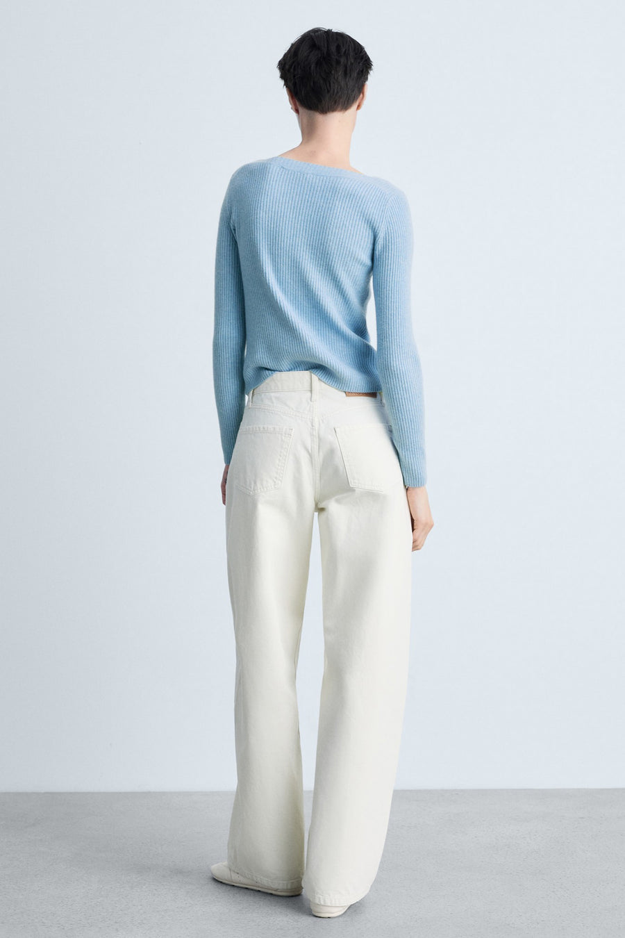 Pull à col rond bleu de MANGO, en tricot côtelé, porté avec un jean blanc à jambes larges.