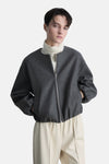 Veste blazer grise zippée de MANGO, style décontracté avec des poches, portée sur un col roulé et un pantalon crème.