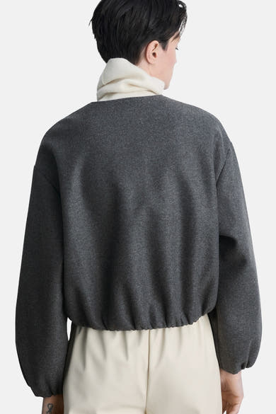 Veste blazer grise de MANGO, vue de dos, portée sur un col roulé blanc et un pantalon écru.