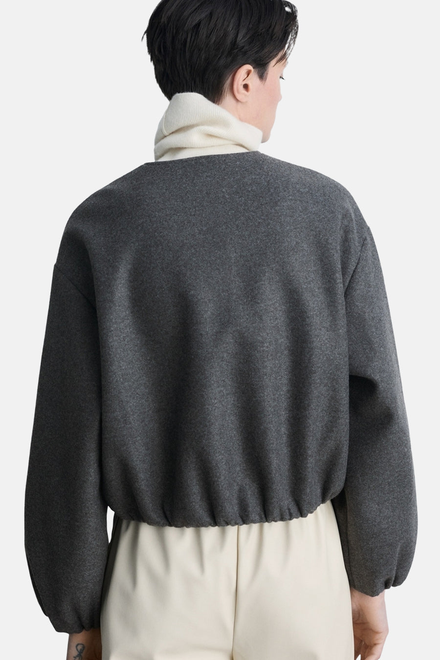 Veste blazer grise de MANGO, vue de dos, portée sur un col roulé blanc et un pantalon écru.
