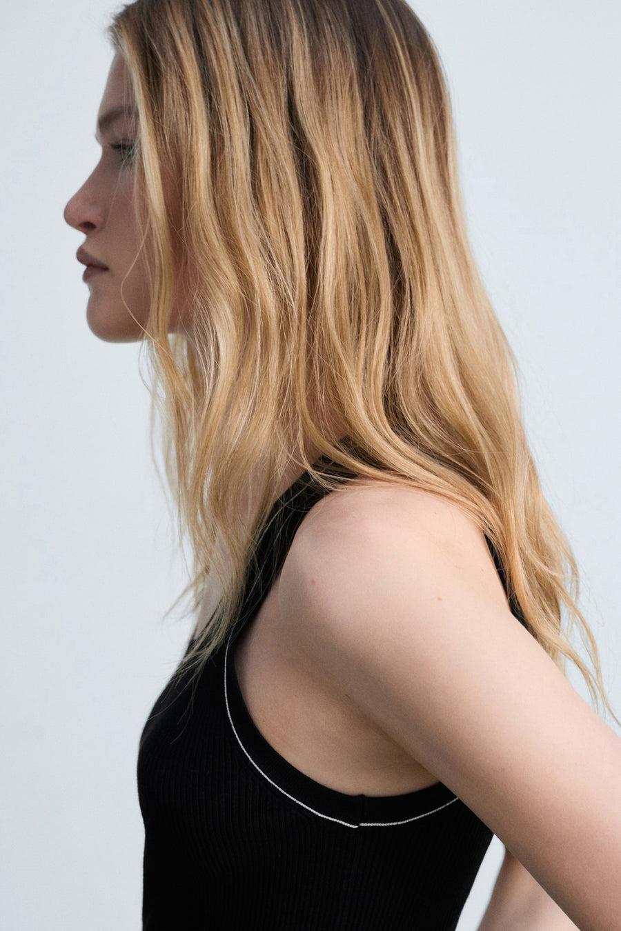 Zwart hemdje van MANGO, gedragen door een model van opzij gezien, met een contrasterende witte bies.