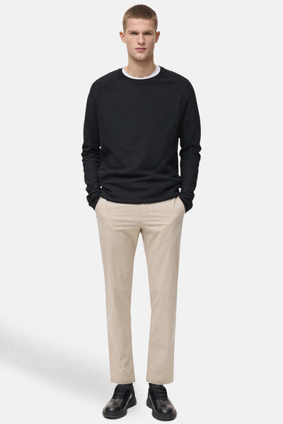 Beige seizoensbroek van MANGO, gedragen met een zwarte trui met lange mouwen en zwarte schoenen.
