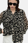 Zwarte blouse met lange mouwen van MANGO, madeliefjespatroon op doorschijnende stof, gedragen met een witte broek.