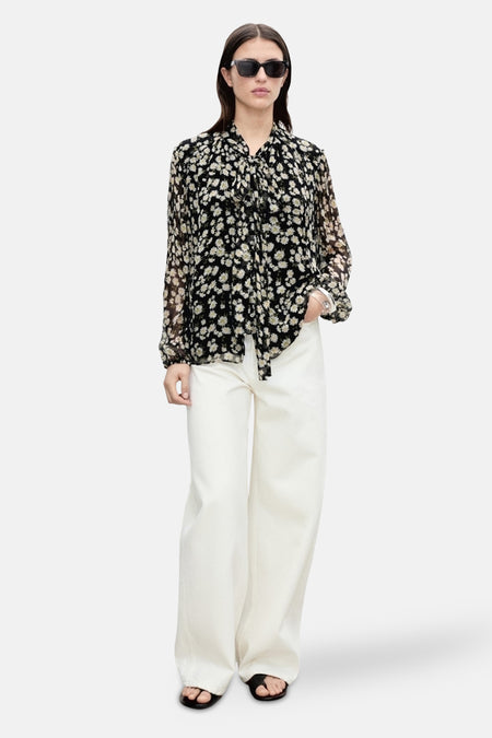 Zwarte blouse met lange mouwen van MANGO met bloemenprint en knoopdetails, gedragen met een witte broek en sandalen.