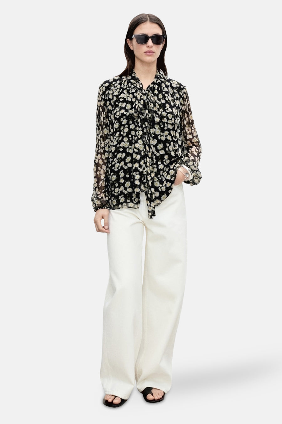 Zwarte blouse met lange mouwen van MANGO met bloemenprint en knoopdetails, gedragen met een witte broek en sandalen.